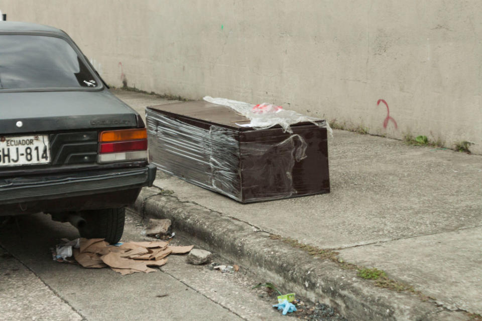 Pictured is a coffin on a footpath next to a car in Guayaquil, Equador.  