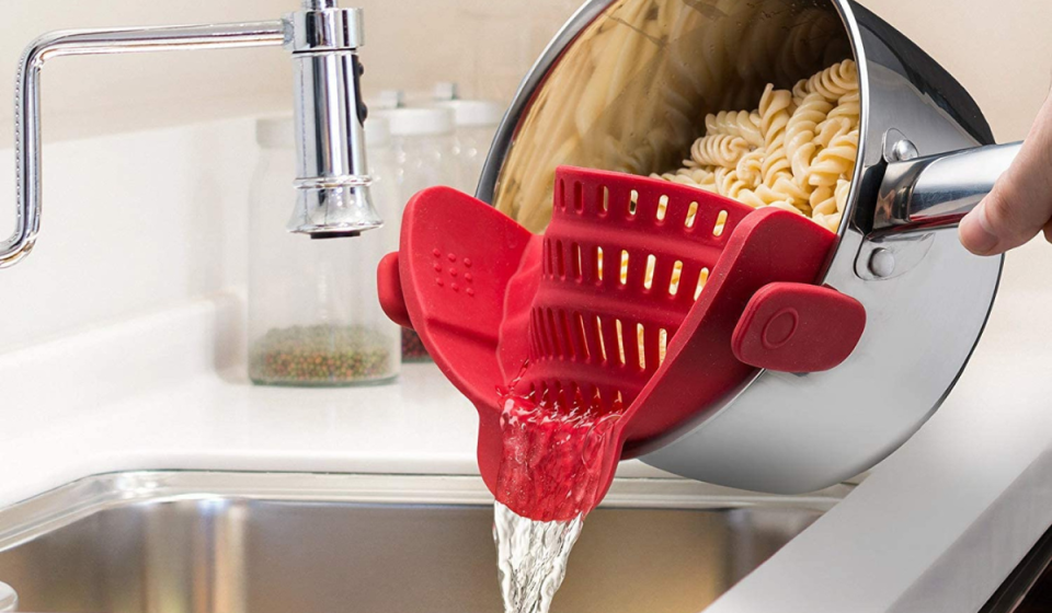 A red colander in a pot full of pasta is being drained.