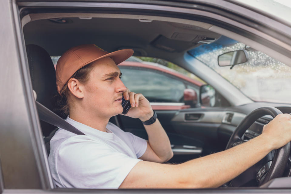 An Uber driver talks on the phone while sitting in his car.