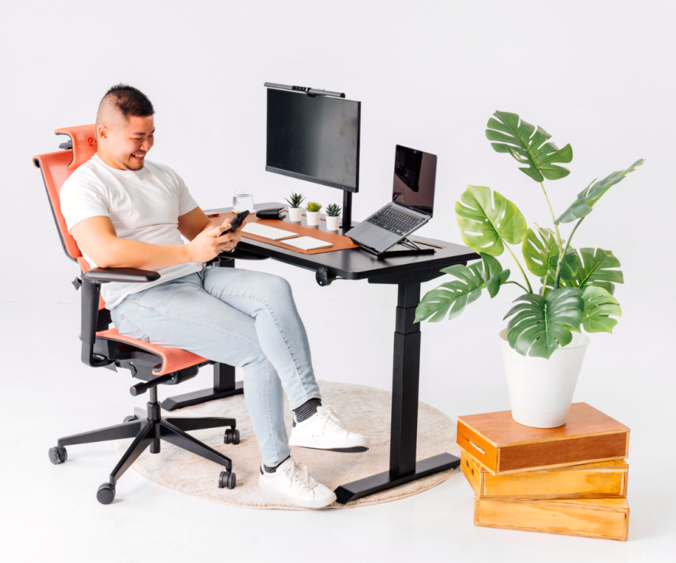 A man sits back on a Supreme chair in a home office environment with a desk, computer and pot plant on the right.