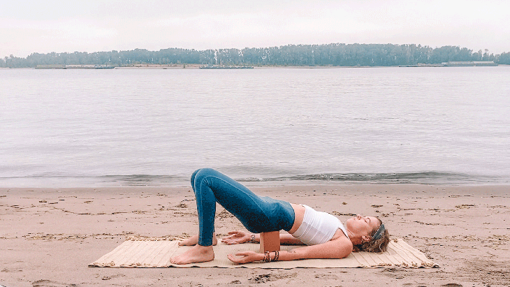 Woman lying on her back with a yoga block beneath her sacrum and her knees bent in a Yin Yoga pose