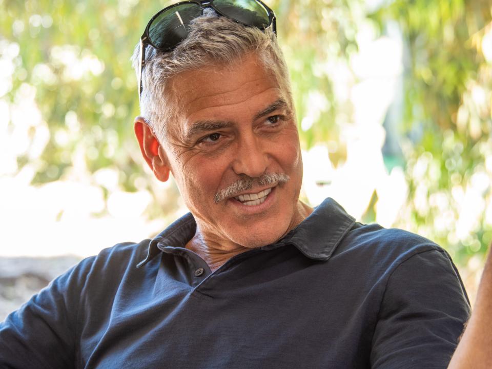 George Clooney wearing a navy polo shirt and sunglasses pushed up to his hairline