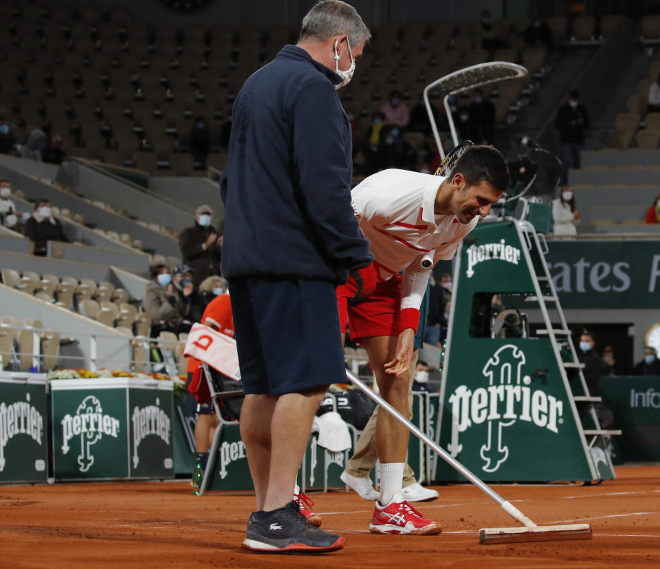 Serbia's Novak Djokovic jokes as he briefly helps clean the court of rain water in the third round match of the French Open tennis tournament against Colombia's Daniel Elahi Galan at the Roland Garros stadium in Paris, France, Saturday, Oct. 3, 2020. (AP Photo/Christophe Ena)