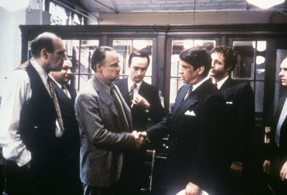 1972:  Marlon Brando shakes hands with Al Lettieri, while Abe Vigoda, Richard S Castellano, John Cazale, James Caan and Robert Duvall look on, in a still from director Francis Ford Coppola's film, 'The Godfather.'  (Photo by Paramount Pictures/Fotos International/Getty Images)