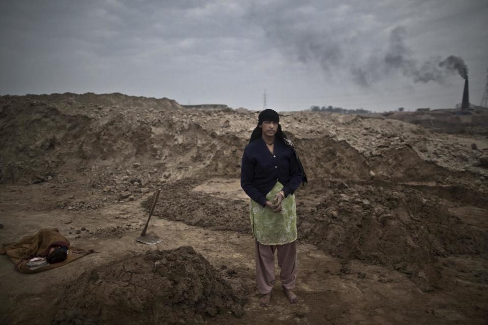 In this Monday, March 3, 2014, photo, with her son Adil, 6, who suffers from a fever, sleeping on the ground wrapped with a shawl, Najma Shahid, 25, a Pakistani brick factory worker, poses for a picture at the site of her work in Mandra, near Rawalpindi, Pakistan. Najma and her husband are in debt to their employer the amount of 80,000 rupees (approximately $800). (AP Photo/Muhammed Muheisen)