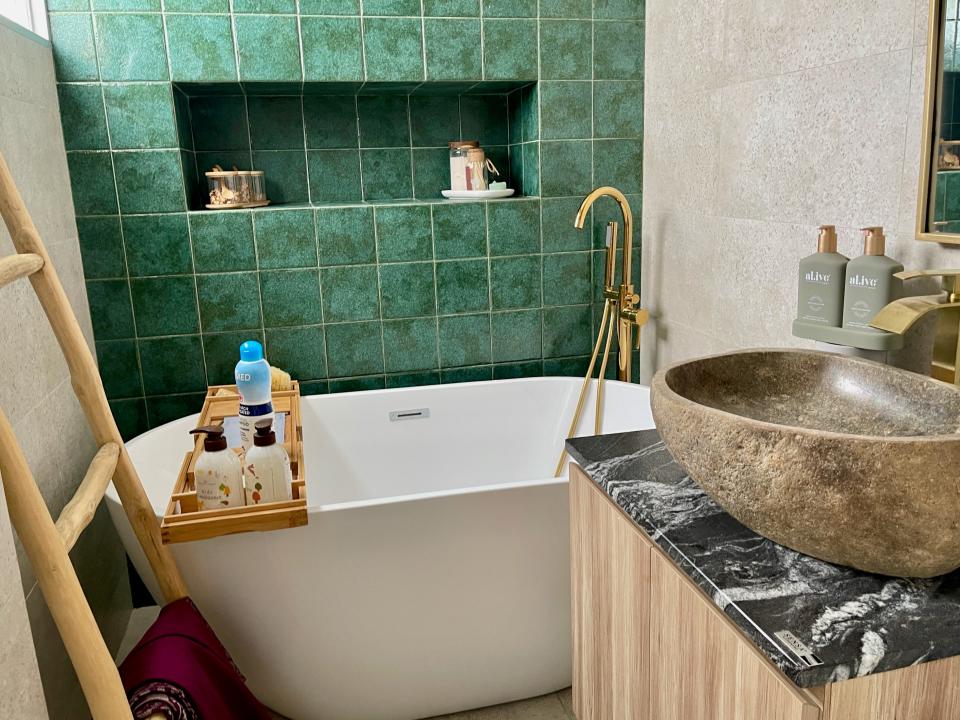 A small bathroom with seaweed-coloured tiles, a small bath, and a large sink on the top of a marble cupboard.