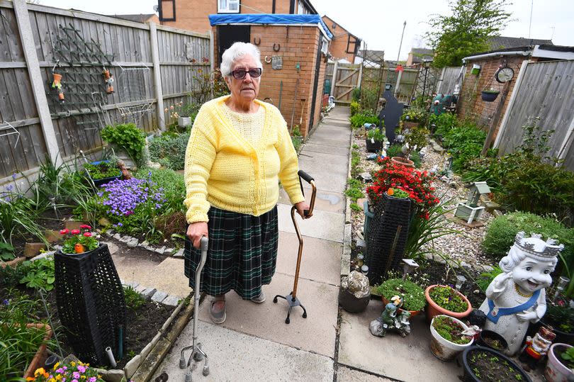 88 year old Patricia Toole in her garden, with her shed that needs repairing