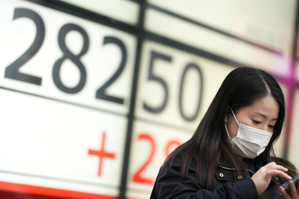 A woman uses her phone in front of monitors showing Japan's Nikkei 225 index at a securities firm while waiting for a traffic light in Tokyo, Thursday, Dec. 1, 2022. Shares have advanced in Asia after a rally on Wall Street spurred by the Federal Reserve chair's comments on easing the pace of interest rate hikes to tame inflation.(AP Photo/Hiro Komae)