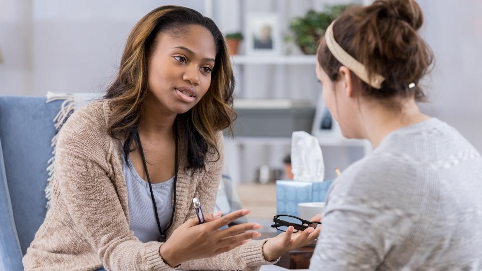 Serious female counselor gestures while talking with Caucasian female client.