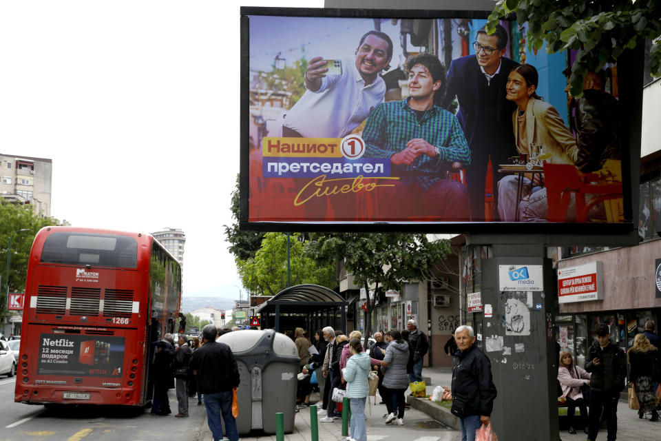 People wait for a bus under an election poster of Stevo Pendarovski, incumbent President and a presidential candidate backed by the ruling social democrats (SDSM), in a street in Skopje, North Macedonia, on Monday, April 22, 2024. Voters go to the polls in North Macedonia on Wednesday for the first round of presidential elections, the seventh such election since the Balkan country gained independence from the former Yugoslavia in 1991, where seven candidates are vying for the largely ceremonial position. (AP Photo/Boris Grdanoski)