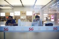 People wearing face masks are seen next to 5G signs on a Huawei store at a shopping mall, in Beijing