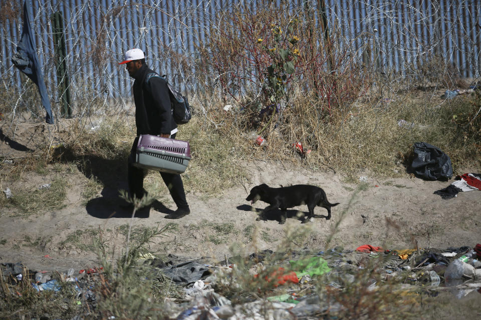 A migrant carries a pet transporter as a dog follows along the U.S. border wall, seen from Ciudad Juarez, Mexico, Wednesday, Dec. 27, 2023. (AP Photo/Christian Chavez)