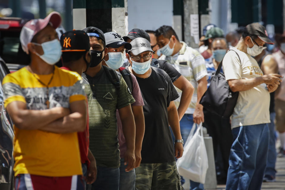 Pedestrians wearing protective masks wait in line for food donations during the COVID-19 pandemic, Tuesday, June 23, 2020, in the Corona neighborhood of the Queens borough of New York. (AP Photo/John Minchillo)