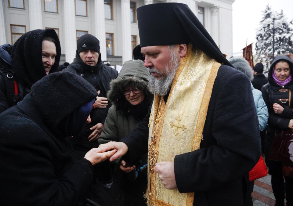 An Orthodox believer kisses the hand of a priest of the Ukrainian Orthodox Church of Moscow Patriarchy during a protest against the creation of a Ukrainian independent church, in front of the parliament building in Kiev, Ukraine, Thursday, Dec. 20, 2018. (AP Photo/Efrem Lukatsky)