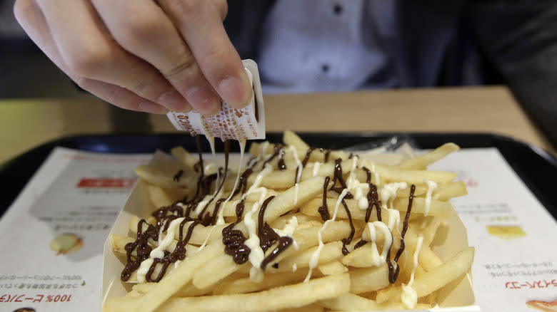 person drizzling sauce on fries