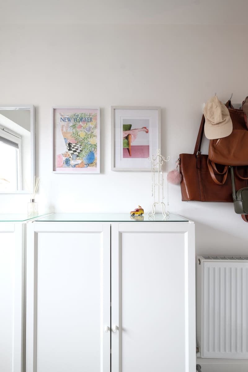 white cabinets with glass top, hook with hats and bags hanging and framed art above cabinets