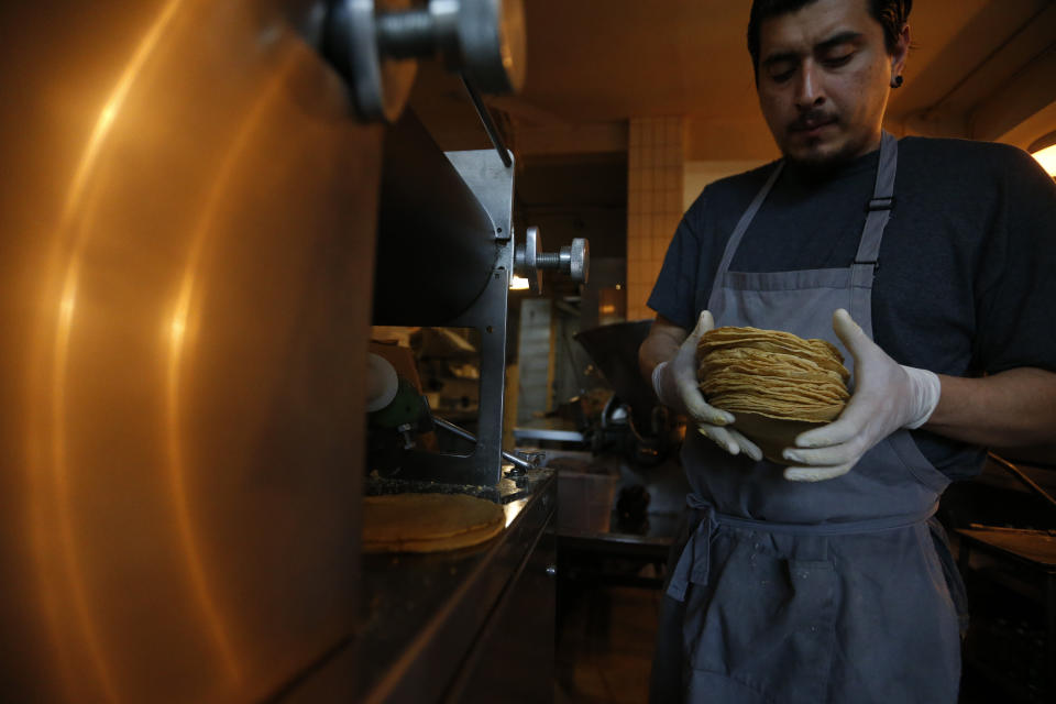 El chef Jesús Saldívar saca las tortillas recién hechas de la máquina para hacer tortillas en el Molino de El Pujol en el vecindario de Condesa de la Ciudad de México, el martes 9 de abril de 2019. (AP Foto / Rebecca Blackwell)