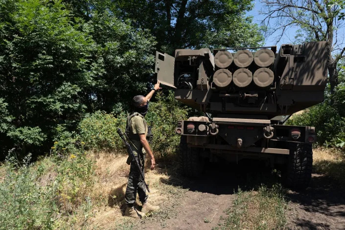 A Ukrainian solider shows the rockets on a HIMARS vehicle between some trees