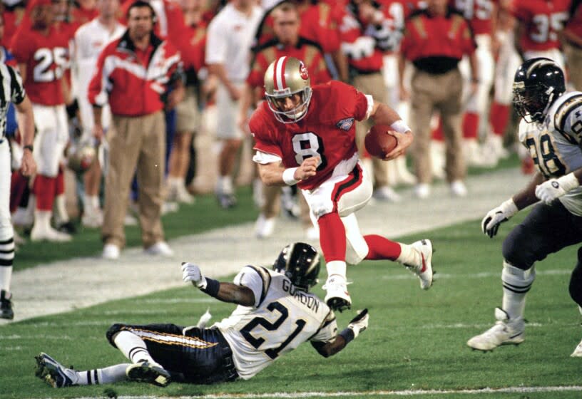 FILE - In this Jan. 29, 1995, file photo, San Francisco 49ers' quarterback Steve Young (8) runs over San Diego's Darrien Gordon (21) for a first down during the first quarter of Super Bowl XXIX at Joe Robbie Stadium in Miami. The NFL became a truly booming business in the 1990s, with multi-billion-dollar TV contracts, expansion to 30 teams, and a late-decade wave of new stadiums. Players began to pick up a bigger share of the wealth, with the dawn of unrestricted free agency. The results on the field were largely dominated by the NFC, with Emmitt Smith and the Dallas Cowboys, Young and the 49ers, and Brett Favre and the Green Bay Packers enjoying the most success. (AP Photo/Andrew Innerarity, File)