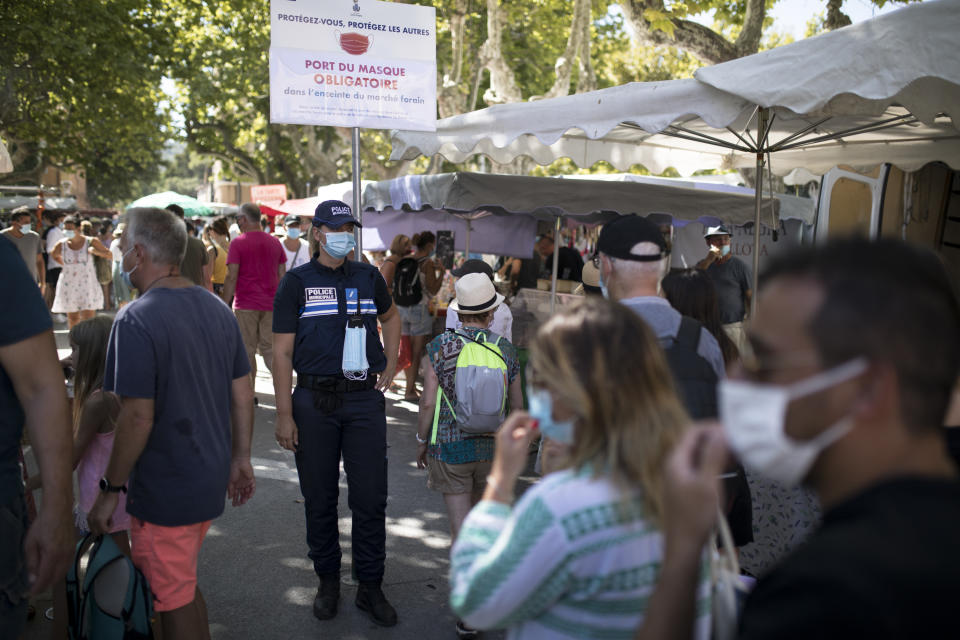 Municipal police watch that pedestrians wear the mandatory facemasks in Saint-Tropez, southern France, Saturday Aug 8, 2020. The glamorous French Riviera resort of Saint-Tropez is requiring face masks outdoors starting Saturday, threatening to sober the mood in a place renowned for high-end, free-wheeling summer beach parties. (AP Photo/Daniel Cole)