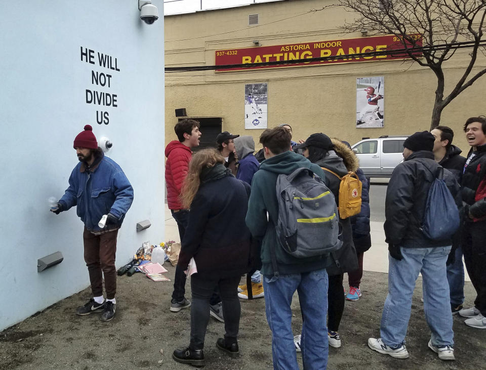 Actor Shia LeBeouf, left, stands in front of a live-steam camera with the words "HE WILL NOT DIVIDE US" posted on a wall outside of the the Museum of the Moving Image as members of the public join LeBeouf in chanting the words "He will Not Divide Us" in the Queens borough of New York. LaBeouf has spent the first four days of the Trump presidency swaying, dancing and chanting, along with anyone who wants to join in. The project by LeBeouf and two other artists opened on Jan. 20 and is expected to go for 4 years, or for "the duration of the presidency." (AP Photo/Deepti Hajela)