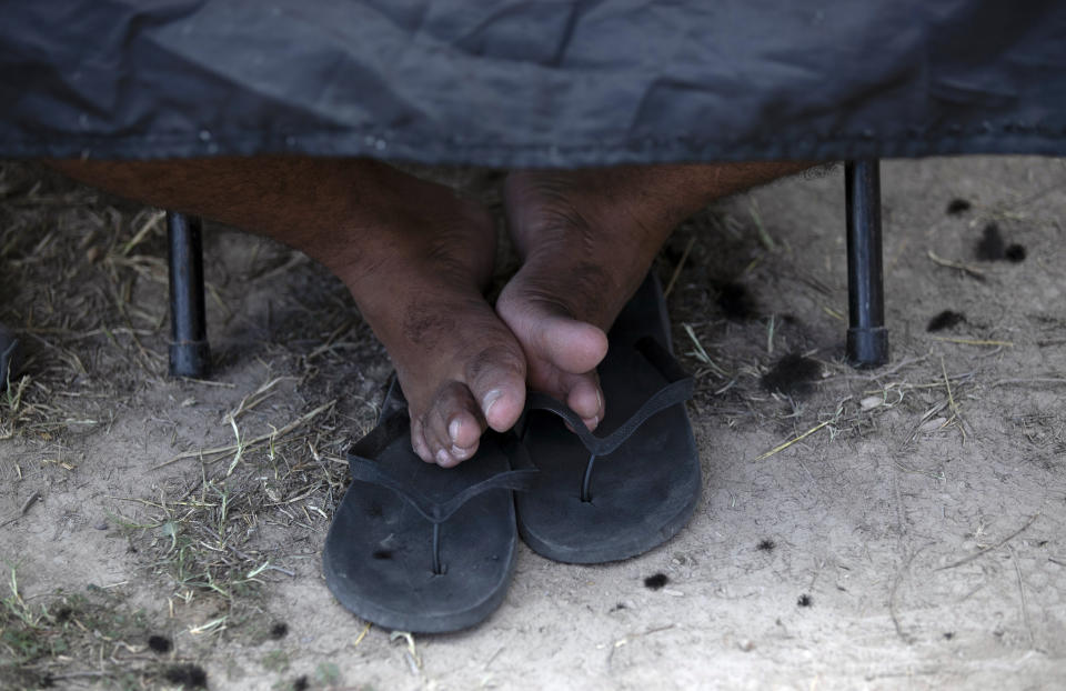 In this Oct. 11, 2019 photo, the feet of a migrant boy rest on his sandals as he sits still for a haircut by a volunteer at a migrant camp near the legal port of entry bridge that connects Matamoros, Mexico with Brownsville, Texas. In years past, migrants moved quickly through this violent territory on their way to the United States. Now, due to Trump administration policies, they remain in Mexico's Tamaulipas state for weeks and sometimes months as they await their U.S. court dates, often in the hands of the gangsters who hold the area in a vice-like grip. (AP Photo/Fernando Llano)