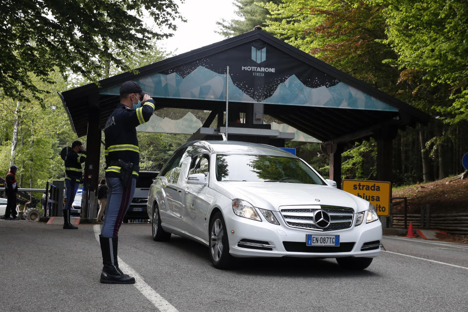 A police officer salutes as a hearse passes by, on the road leading to the Stresa-Mottarone after a cable car of the line collapsed, near Stresa, Italy, Sunday, May 23, 2021. A cable car taking visitors to a mountaintop view of some of northern Italy's most picturesque lakes plummeted to the ground Sunday and then tumbled down the slope, killing at least 13 people and sending two children to the hospital, authorities said. (AP Photo/Antonio Calanni)