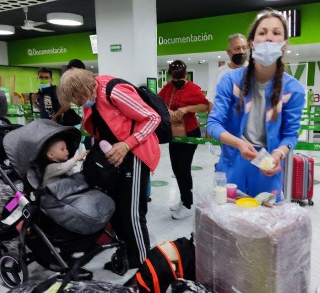 Olya, standing right, mixes formula for her baby Nikol in the middle of an airport, while her mother Tamara talks to the girl.