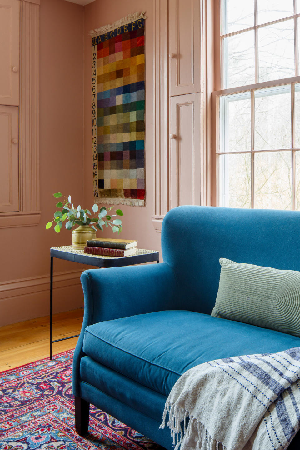 Corner of a pink living room with pink solid shutters, multicoloured wall art and blue sofa