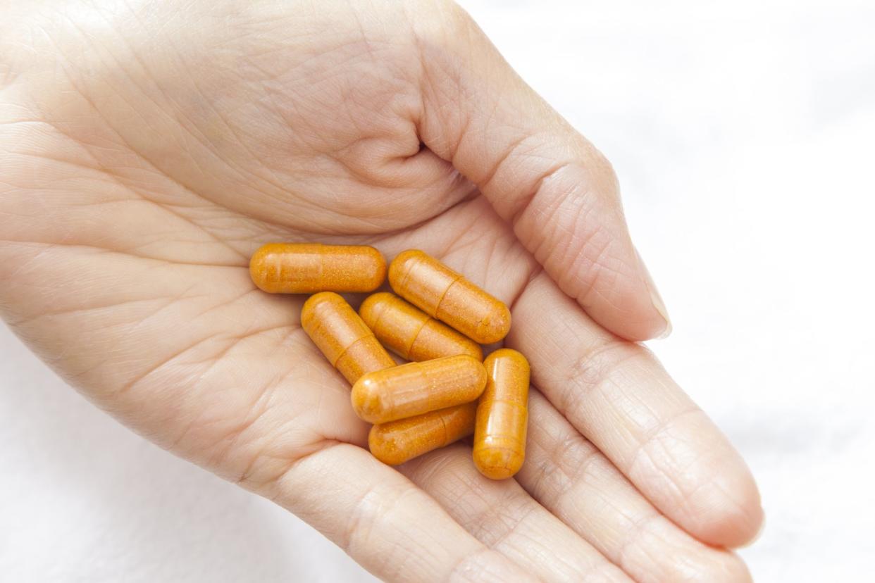 Woman's hand holding orange turmeric vitamin medicine supplement pill capsules