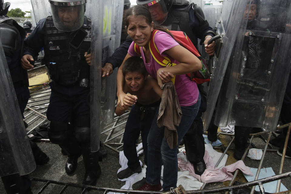 A Honduran migrant mother and child are shielded by Mexican Federal Police from stones thrown by unidentified people, at the border crossing in Ciudad Hidalgo, Mexico, on Friday, Oct. 19, 2018. The mother and child were unsuccessful in their attempt to cross into Mexico and were returned to the Guatemalan side. (AP Photo/Moises Castillo)