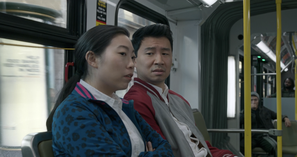 Awkwafina and Simu Liu seated on a bus, having a conversation