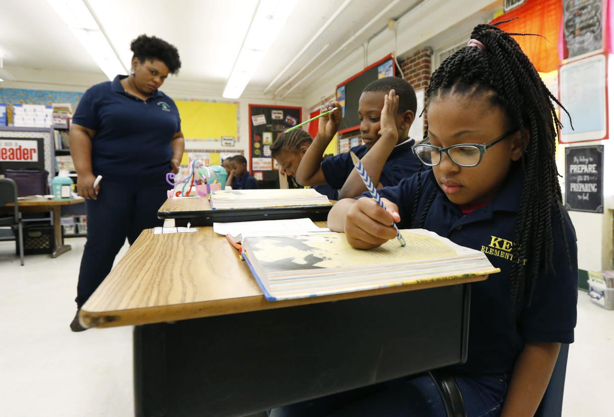 Elize'a Scott, a Key Elementary School third grade student, right, reads under the watchful eyes of teacher Crystal McKinnis, left, Thursday, April 18, 2019, in Jackson, Miss. More than 35,000 Mississippi third graders sat down in front of computers this week to take reading tests, facing a state mandate to "level up" or not advance to fourth grade. And with the bar set higher this year, state and local officials expect more students will fail the initial test, even with efforts to improve teaching. (AP Photo/Rogelio V. Solis)