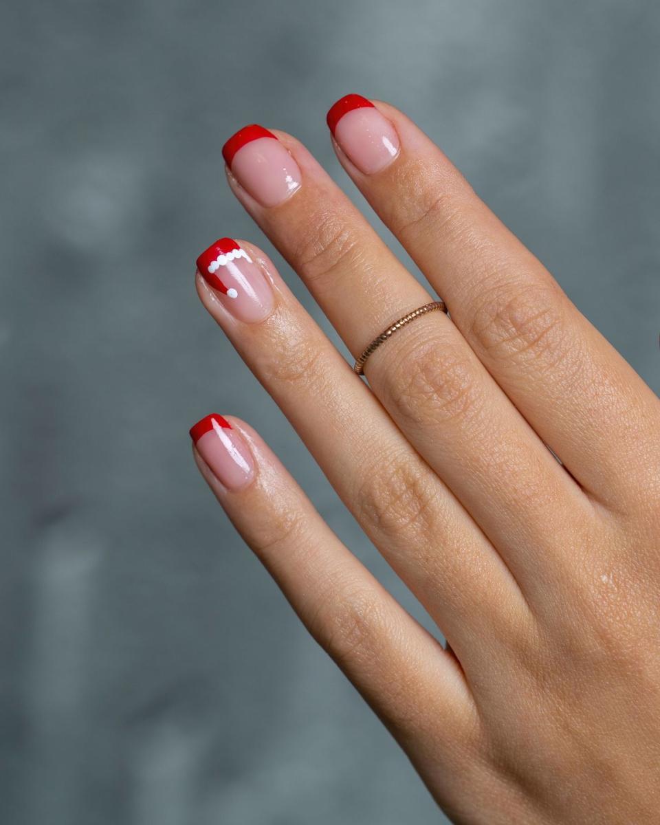 a persons hand with painted nails with red tips and the ring finger has a santa hat painted on