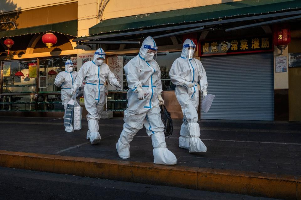 Epidemic control workers in Beijing walk by a closed shop near a community with residents under health monitoring for COVID-19 on Dec. 4.