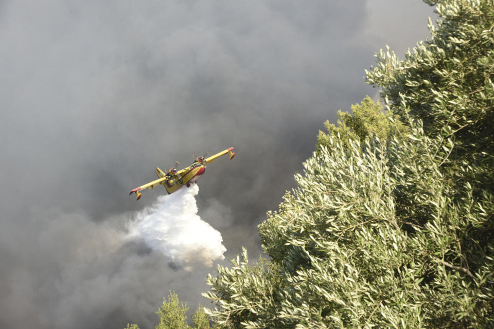 An airplane drops water over a wildfire near Lampiri village, west of Patras, Greece, Saturday, Jul. 31, 2021. The fire, which started high up on a mountain slope, has moved dangerously close to seaside towns and the Fire Service has send a boat to help in a possible evacuation of people. (AP Photo/Andreas Alexopoulos)