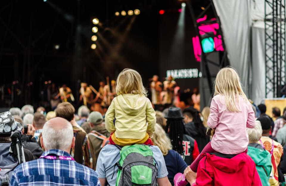 Two children sitting on people's shoulders in the crowd during a performance at a festival. (Photo via Getty Images)