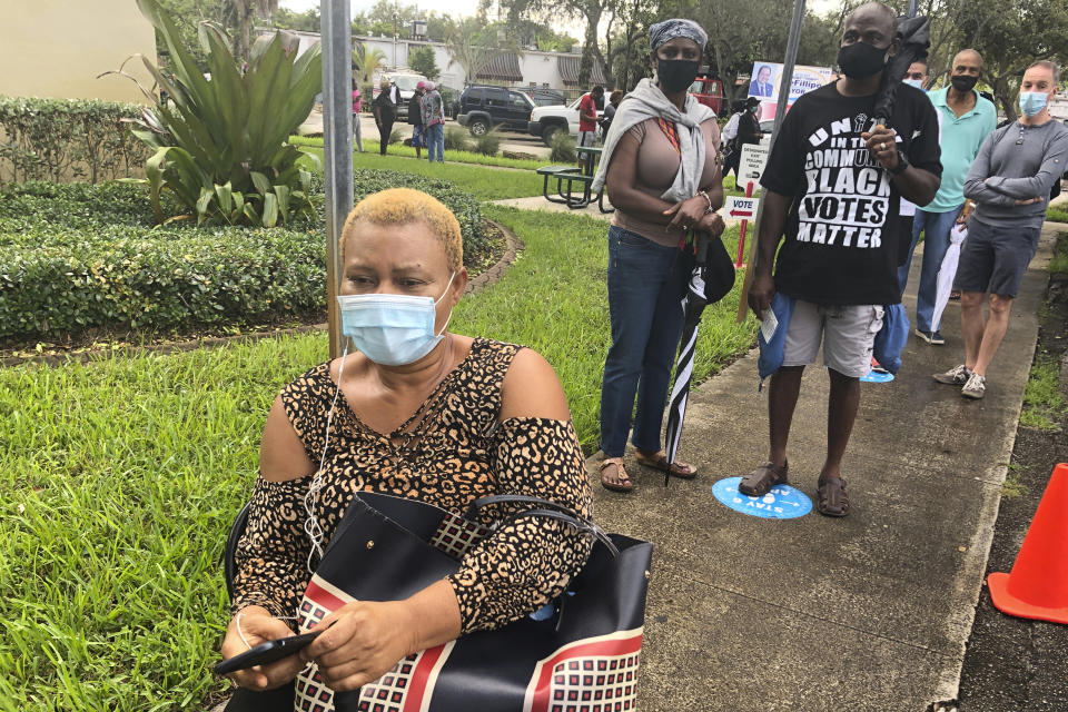 Chinwe Osuji sits in line to vote, Monday, Oct. 19, 2020, in North Miami, Fla. Florida begins in-person early voting in much of the state Monday as the Trump campaign tries to cut into an early advantage Democrats have posted in mail-in votes in the key swing state. (AP Photo/Marta Lavandier)