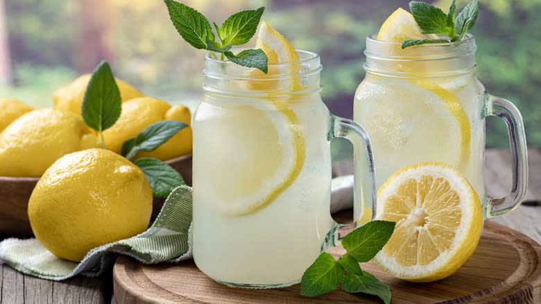 Two glasses of lemonade next to whole lemons