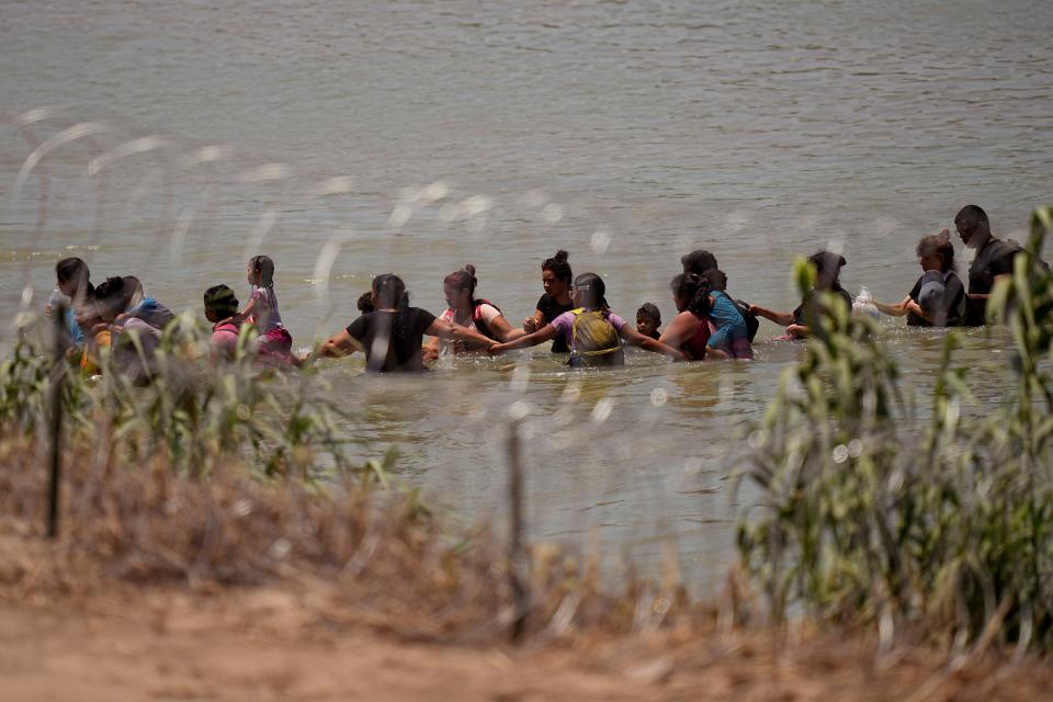 Migrants join hands as they cross the Rio Grande near the site where large buoys are being deployed to be used as a border barrier in Eagle Pass on July 12. The floating barrier is being deployed in an effort to block migrants from entering Texas from Mexico.