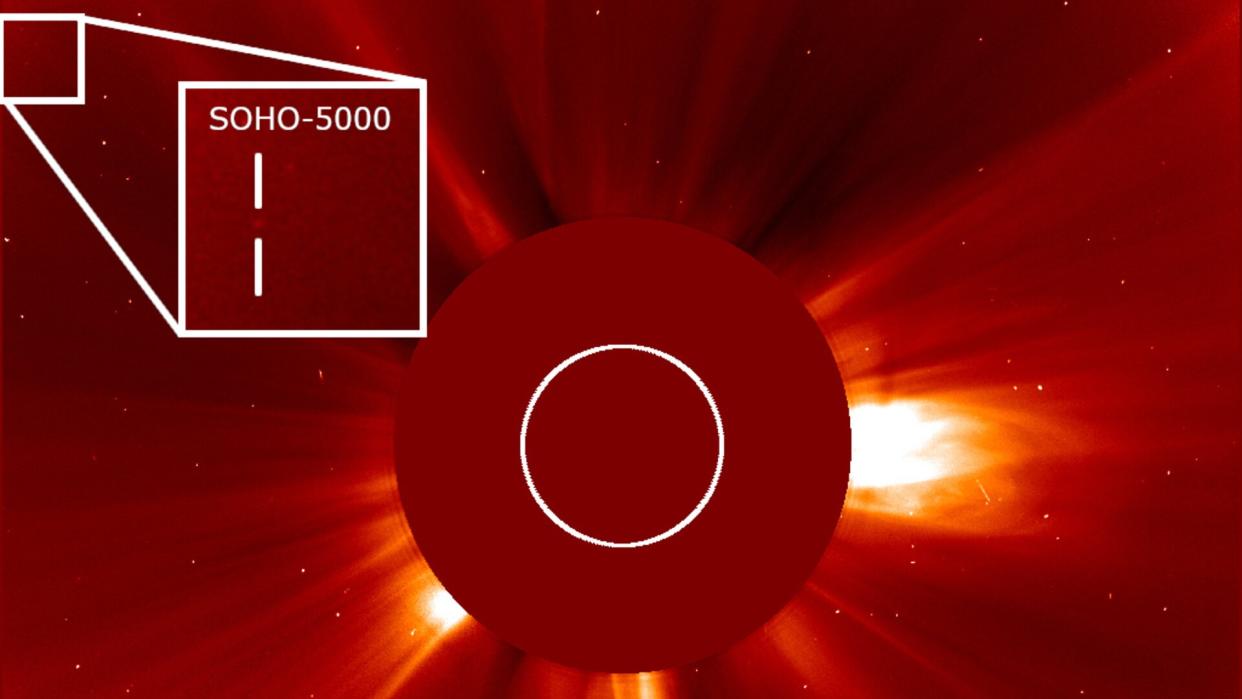  A bright orange circle covers almost the whole image, with a smaller disc in the middle. Out of the smaller disc protrude wisps of the Sun's atmosphere. To the upper right of the inner circle, an inset zooms in on a small square, with vertical lines surrounding a faint smudge. 