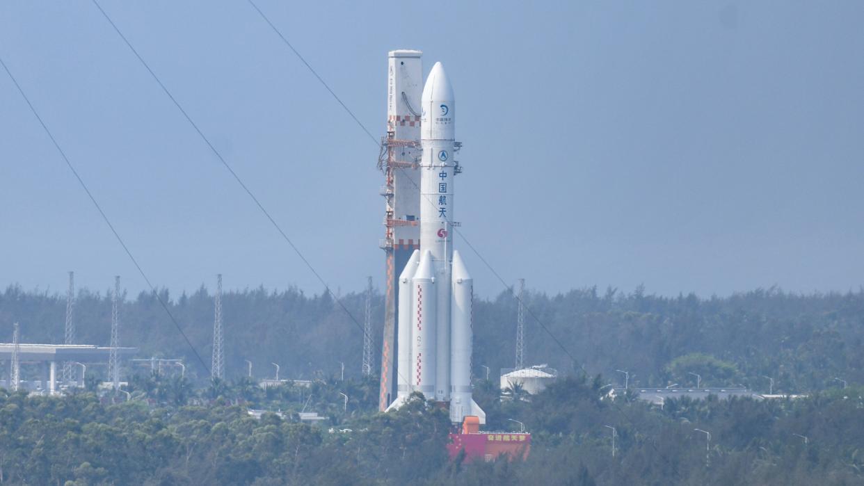  A large white rocket attached to a mobile tower rolls along a road surrounded by palm trees. 