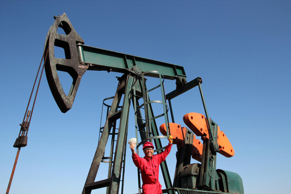 Oil worker holding cash in front of an oil pump.