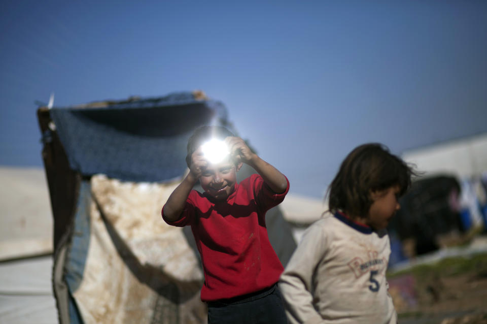 In this Friday, April 4, 2014 photo, a Syrian boy uses a small piece of mirror as a light reflector as he plays with others in an unofficial refugee camp on the outskirts of Amman, Jordan. Some Syrians have set up informal camps to flee the tensions at Zaatari, the region's largest camp for Syrian refugees, and to be closer to job opportunities. (AP Photo/Khalil Hamra)