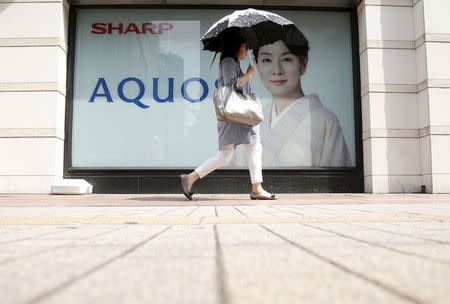A woman holding her umbrella walks past an advertisement poster for Sharp Corp's Aquos outside an electronics shop in Tokyo, Japan, July 31, 2015. REUTERS/Yuya Shino