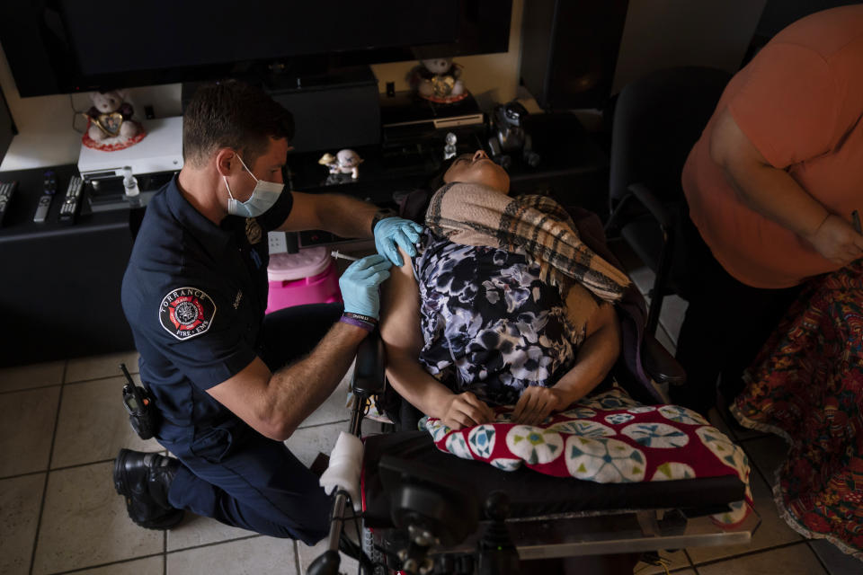 Torrance firefighter Trevor Borello, left, administers the second dose of the Pfizer COVID-19 vaccine to Barbara Franco, who has muscular dystrophy, at her apartment, Wednesday, May 12, 2021, in Torrance, Calif. Teamed up with the Torrance Fire Department, Torrance Memorial Medical Center started inoculating people at home in March, identifying people through a city hotline, county health department, senior centers and doctor's offices, said Mei Tsai, the pharmacist who coordinates the program. (AP Photo/Jae C. Hong)