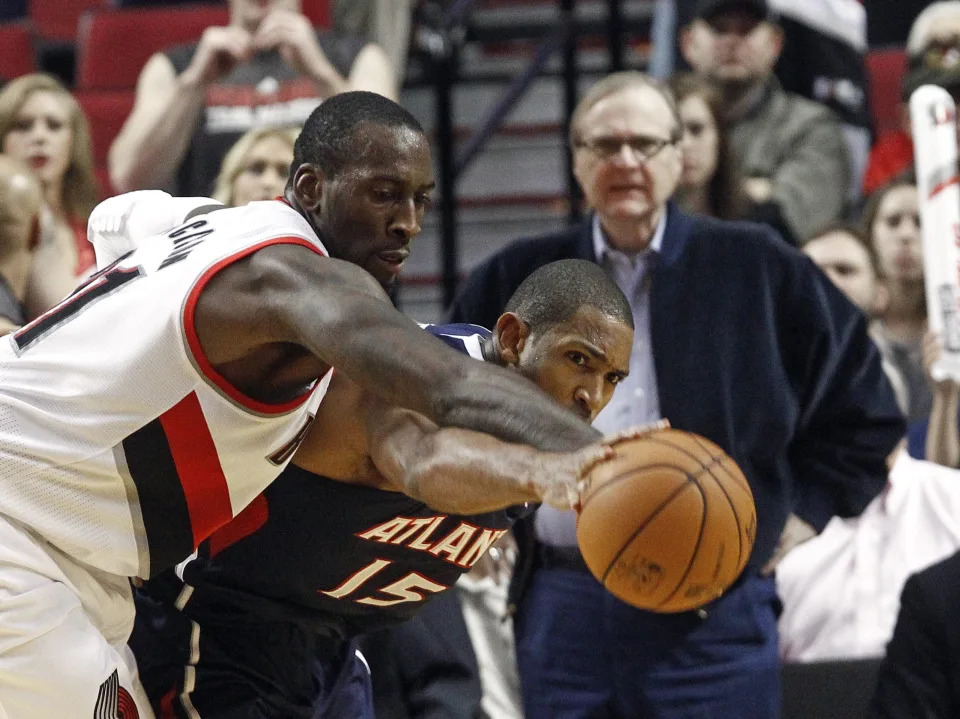 Two basketball players reach for a basketball as Paul Allen looks on in the background