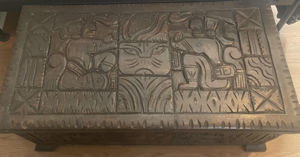 Carved wooden chest with intricate designs and animals, displayed indoors as a unique furniture piece