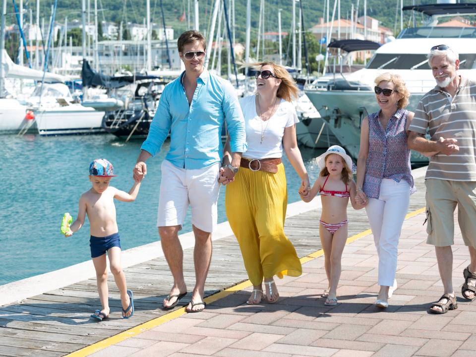 A three-generation rich family strolls down a boat dock on a sunny day