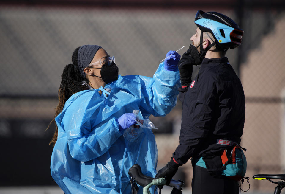 A medical technician performs a nasal swab test on a cyclist queued up in a line with motorists at a COVID-19 testing site near All City Stadium Thursday, Dec. 30, 2021, in southeast Denver. With the rapid spread of the omicron variant paired with the Christmas holiday, testing sites have been strained to meet demand both in Colorado as well as across the country. (AP Photo/David Zalubowski)